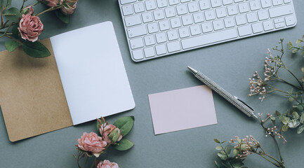 Schreibtisch mit Tastatur, Kugelschreiber, Karte, Notizheft, dekoriert mit rosa Kunstrosen