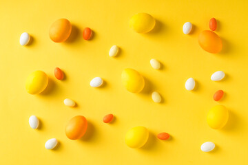 Yellow easter eggs with colorful candies on yellow background.