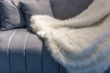 White fur fluffy plaid on a gray velor sofa. Coziness and comfort in interior decoration. Close-up....