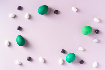 Green easter eggs with colorful candies on purple background. Blank copy space on center.