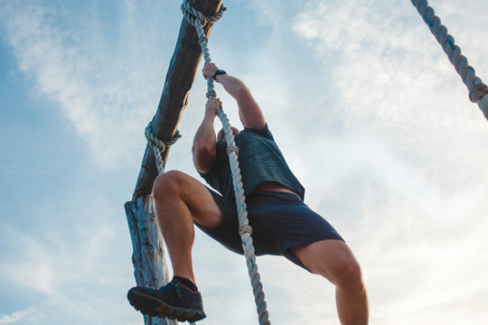 Below-view of a strong male pulling himself up a rope against blue sky