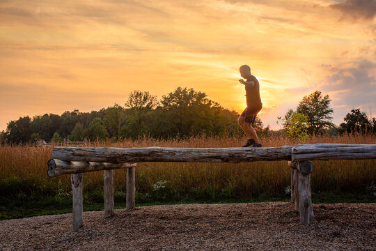 A man walks across balance beam outdoors silhouetted against sunset