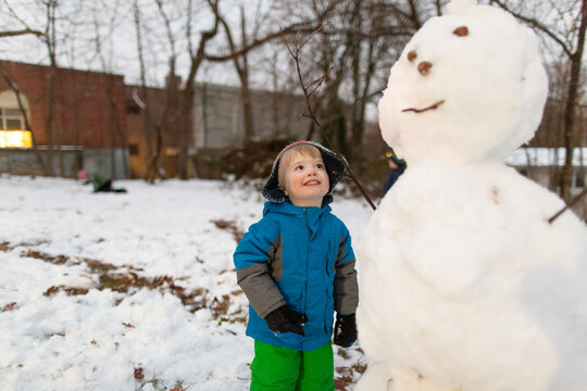 Toddler boy smiling while looking up at large snowman's face in winter