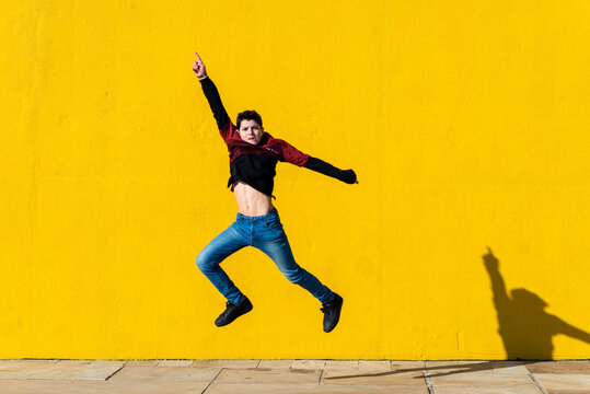 Smiling young teen jumping against yellow wall in a sunny day