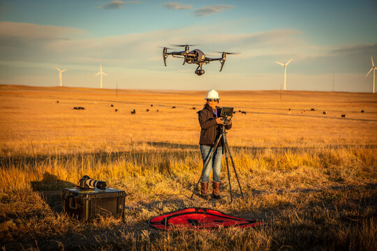 Female drone pilot flies in a wind farm at sunrise