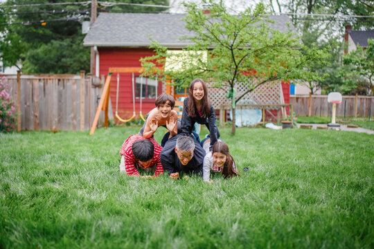 A smiling family are stacked up in human pyramid in backyard play