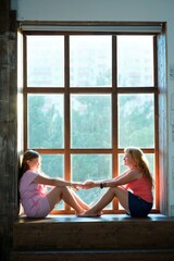 A girl and her mother are indoors near a large panoramic window.
