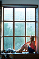 The girl is sitting in a room near a large panoramic window.