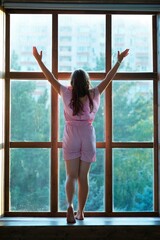The girl is standing in the room near a large panoramic window.