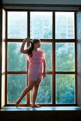 The girl is standing in the room near a large panoramic window.