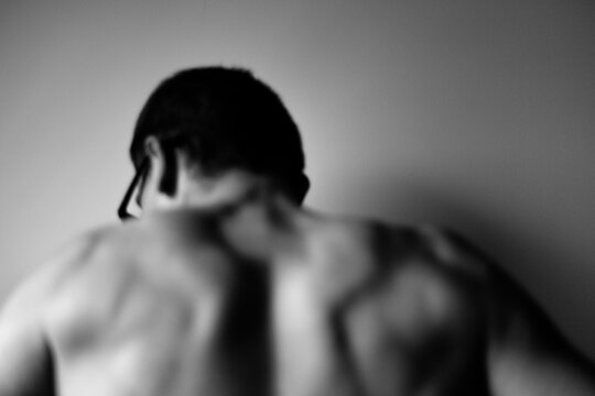 Close-up back view of young man standing against wall. Nude B&W