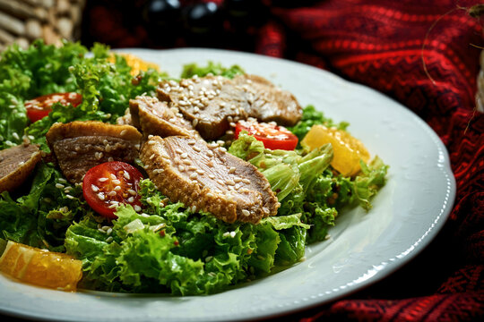 Salad with duck breast, tomatoes and sauce in a white plate.