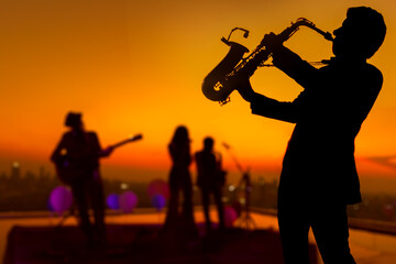 Silhouette saxophone musician man showing on blurry jazz trio band and sunset cityscape background....