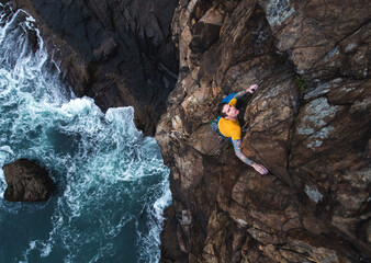 Man rock climbing on seaside cliff with waves crashing below