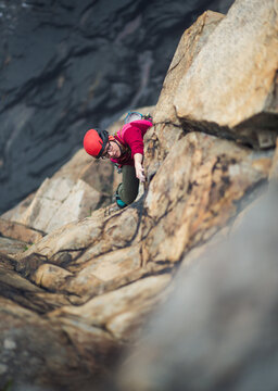 Woman wearing red trad climbing on lead with belayer below