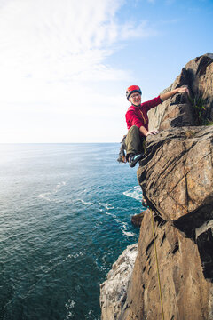 Woman wearing red trad climbing on lead with ocean below