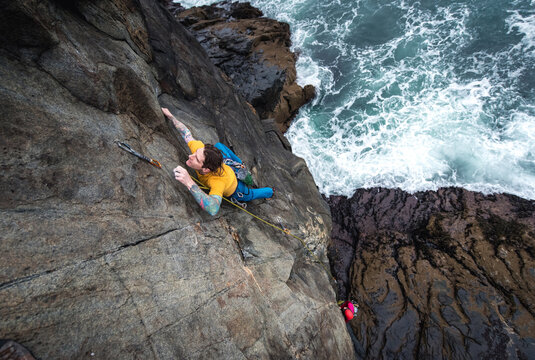 Man rock climbing on seaside cliff with waves crashing below