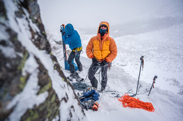 Men preparing gear for winter ski-mountaineering in puffy jacket