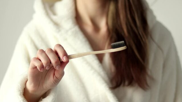 Environmentally friendly bamboo toothbrush in a woman's hand in close-up. A girl in a soft beige dressing gown.