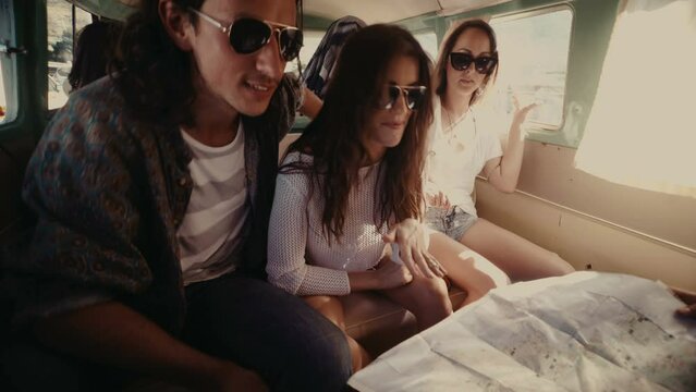 Group of friends looking for the way on the map during a road trip sitting in a vintage van
