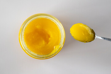 Glass jar and spoon of Ghee butter on white background, closeup.