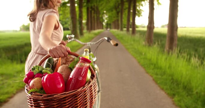Cropped image of a woman walking on a road in a park with her bicycle and a basket of organic vegetables fresh from the market