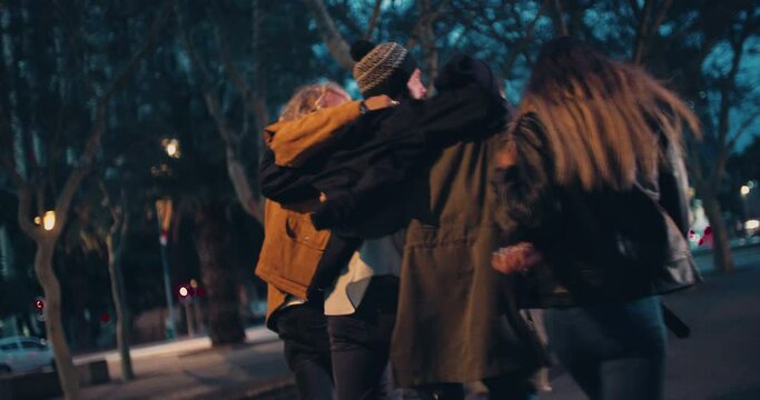 Young happy couples in winter outfits embracing while taking a night walk outside in the city