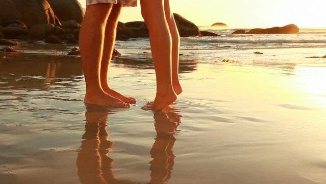 Close-up of a couple's feet feet on the beach, she's is giving him a kiss