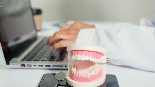 Dentist doctor or nurse woman in uniform typing information medical history form into laptop computer for record document data report, Teeth model on desk, dentistry concept