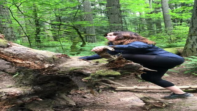 Handheld shot of woman climbing on log in forest