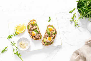 Tuna toast. Open sandwiches with whole grain bread, canned tuna, boiled egg, avocado and arugula. Top view