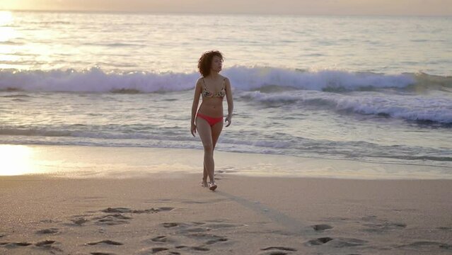 Full length handheld shot of woman in bikini walking at beach during sunset