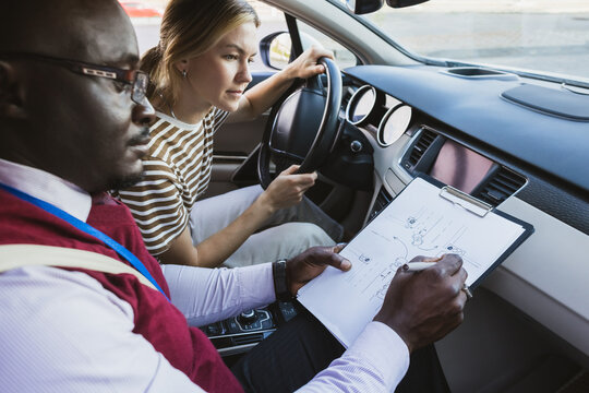 Driving school concept. A car instructor teaches a young woman how to drive. Teaching the rules of the road and driving a vehicle