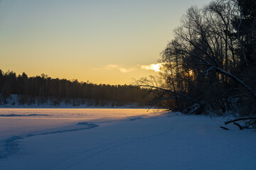Frozen river covered with ice during sunset. Surrounded by trees growing along the banks.