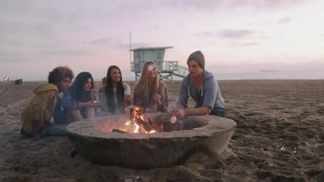 Friends roasting marshmallows around beach campfire