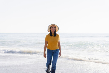 Beautiful latina woman with a hat enjoys walking barefoot on the beach on a sunny spring day.