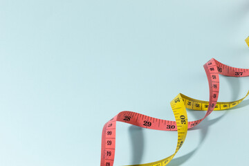 Close up of a pink and yellow measure tape on cyan background. Top view.