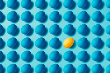 Blue easter eggs on blue background.  One yellow egg standing out. Table top flat lay shot.