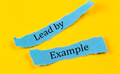 LEAD BY EXAMPLE text on a blue pieces of paper on yellow background, business concept