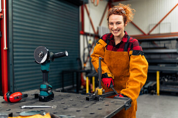 A young mechanical engineer works in the workshop and smiles at the camera, the owner of her...