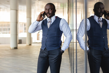 Portrait of handsome afro american businessman using phone in suit against modern building...