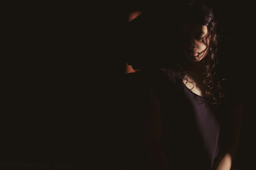 young woman on black background with light and shadow on sad face