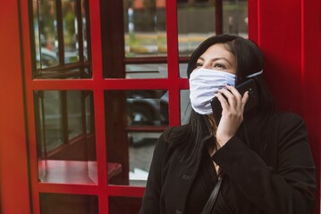 Beautiful hispanic woman talk on the phone with mask for new normal