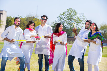 Group of happy young Indian people celebrating holi festival at park outdoor, Playful adult male...