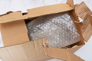 Damaged and torn open cardboard box for transporting things. Top view. Close-up. Bubble wrap keeps things and utensils in transit.