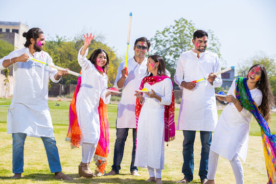 Group of happy young Indian people celebrating holi festival at park outdoor, Playful adult male and friends with colorful paint faces playing with gulal.