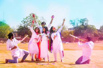 Group of happy young Indian people celebrating holi festival at park outdoor, Playful adult male...