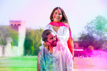 Cheerful young Indian couple playing with colorful powder color or gulal celebrating holi festival...