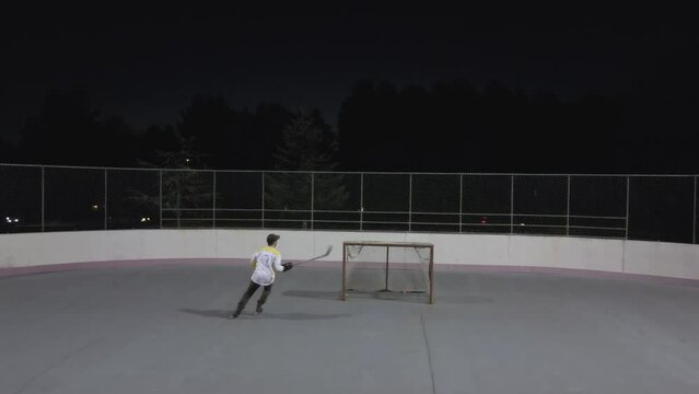 A hockey player skating and shooting a puck at an empty net