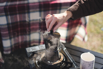 Woman prepares coffee outdoors from a geyser coffee pot. Girl prepares coffee outdoors.
